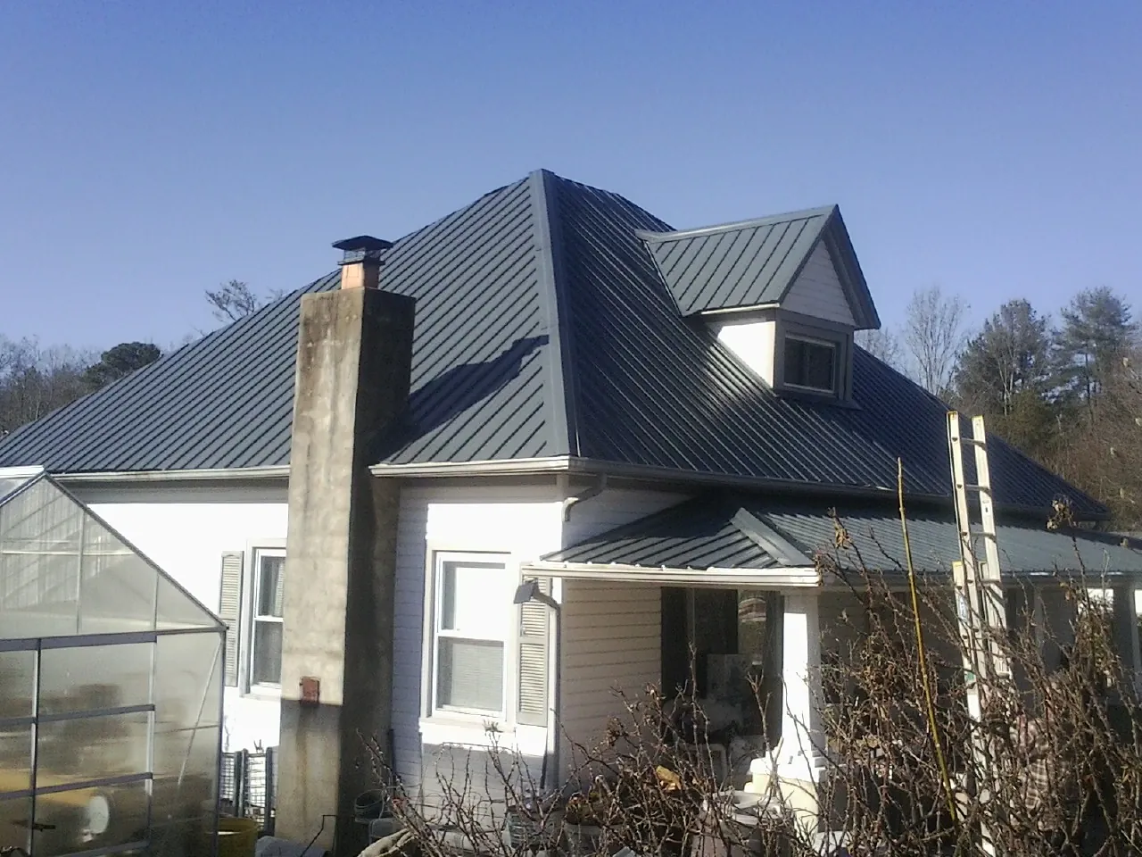Dark blue standing seam metal roof on a white farmhouse with dormer — Slate & Tile Roof Repair by Roofing Brothers in Murray City