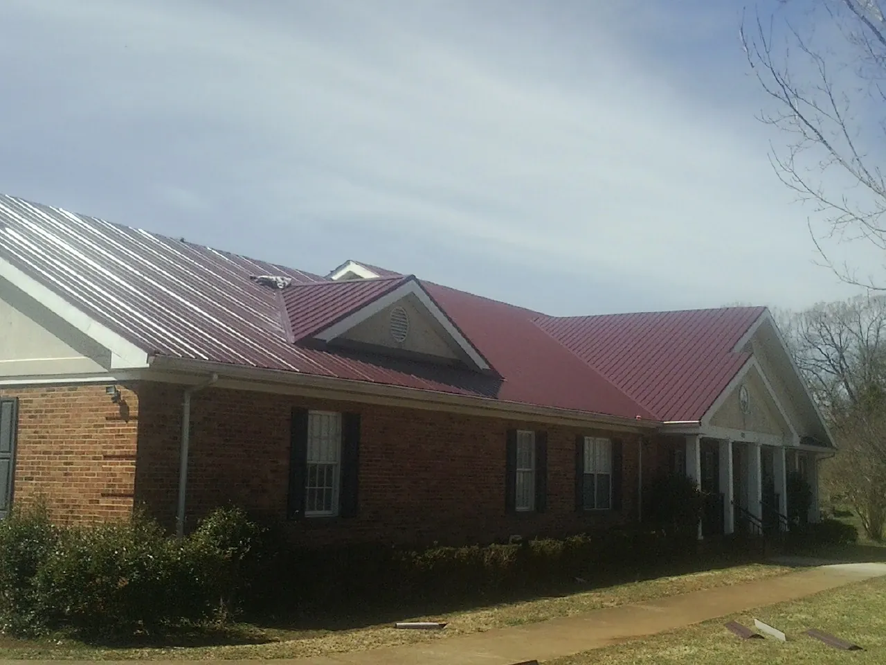 Red metal roof with gabled entries on a long brick building, from a Hail Damage Roof Repair job in Murray City