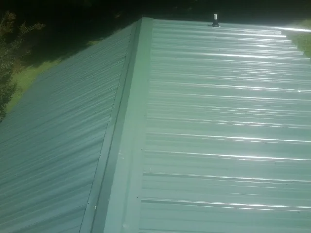 New green metal panels meeting at the ridge of a roof — Flat Roof Repair work by our crew in Murray City