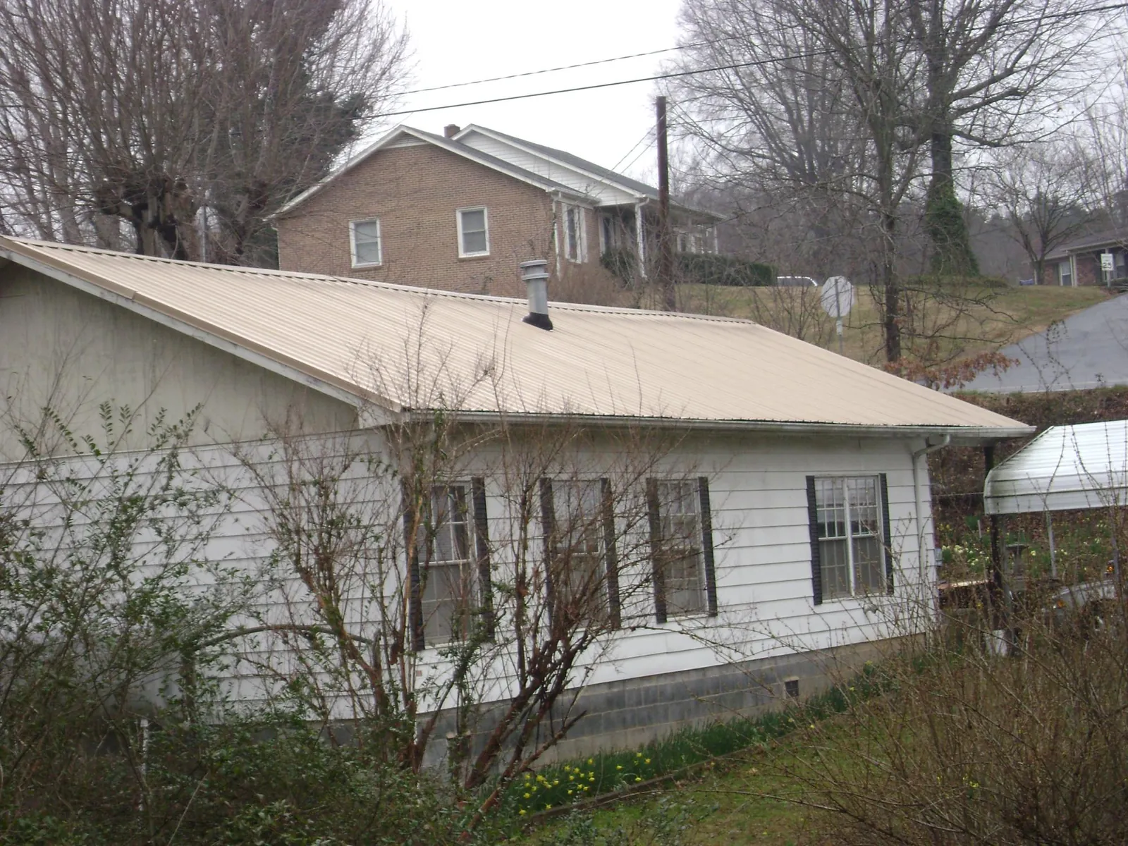 Tan metal roof on a white sided house set into a hillside — Commercial Roofing by Roofing Brothers in Murray City