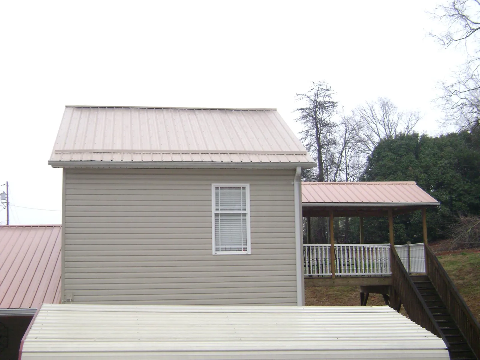 Tan metal roofs on a two story addition and attached porch, from a Roof Replacement job in Murray City